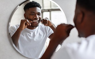 Man smiling while flossing his teeth in bathroom